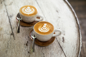 Two cups of cappuccino with latte art on saucer with spoons white wooden background