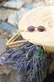 Fototapeta Lawenda - Straw bag filled with fresh lavender flowers and retro sunglasses. Selective focus.