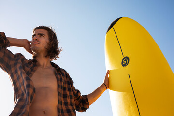 Portrait of handsome surfer with his surfboard. Young man with a surfboard on the beach.