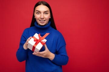 Shot of attractive positive smiling young brunette woman isolated over colourful background wall wearing everyday trendy outfit holding gift box and looking at camera