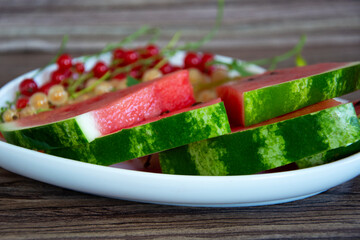 Watermelon and currant berries on a wooden plan. Slices of ripe watermelon are in a white plate.