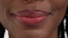 Close up of an African woman's mouth licking her upper lip and then smiling with her mouth closed.
