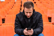 © Alrandir - portrait of a serious man in a black jacket looking into a smartphone against the background of the stadium chairs