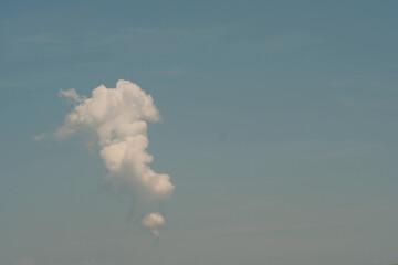 single puffy whiote cloud in hazy blue summer sky with negative space for copy
