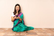 © luismolinero - Young Indian woman sitting on the floor sending a message with the mobile