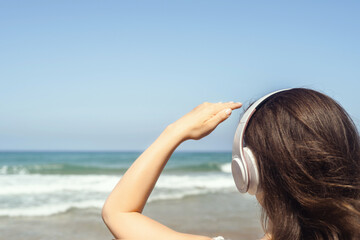 Alone woman on a beach in headphones listen music looking on the sea. Female relaxation at summer vacation. Back view