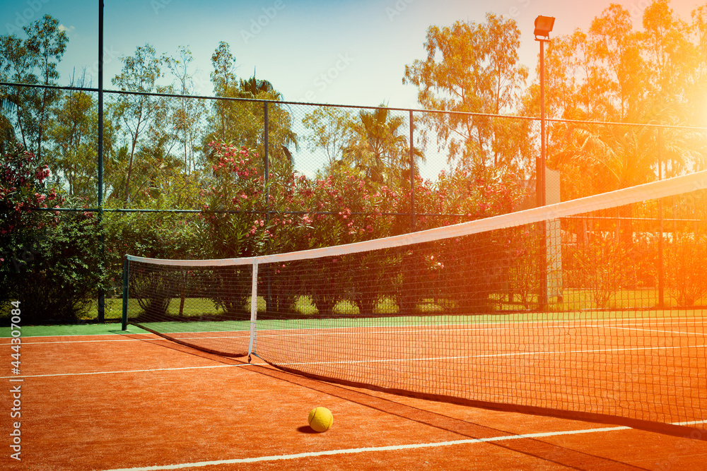 Wide angle photo of artificial grass tennis court with tennis ball during sunset. Competitive individual sports concept. - obrazy, fototapety, plakaty 