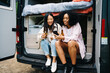 © ADDICTIVE STOCK - Diverse girlfriends with beer using mobile phone in van