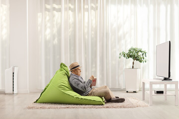 Canvas Print - Elderly man sitting in a bean-bag chair, watching tv and eating popcorn in a living room