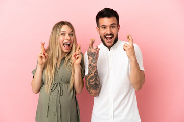 Wall Mural - Pregnant woman and man over isolated pink background with fingers crossing