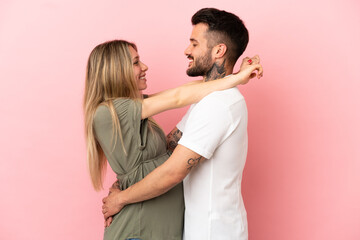 Wall Mural - Pregnant woman and man over isolated pink background hugging