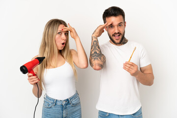 Poster - Couple holding a hairdryer and brushing teeth over isolated white background has just realized something and has intending the solution