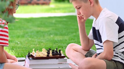 Wall Mural - Brother and sister playing chess in the backyard with green lawn