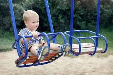 Happy, smiling child is swinging on a swings in a park at summer