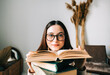 © nikkimeel - Portrait of young caucasian woman college student in eyeglasses with stack of books, looking at camera.
