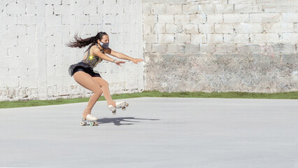 Latin teenager with a mask, performing a figure skating figure on wheels, falling from an axel jump