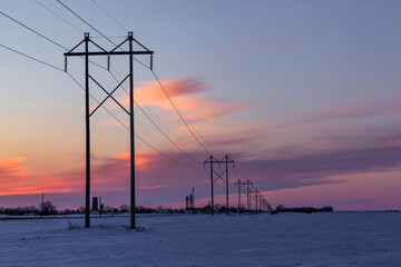  Row of power line poles near a small town at sunset in the Winter in rural Minnesota, USA
