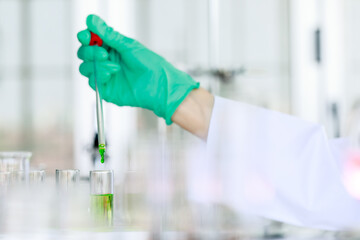 Wall Mural - Crop unrecognizable scientist in lab coat and gloves with pipette pouring green liquid into flask while conducting chemical experiment in laboratory.