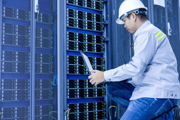 Wall Mural - A man with a laptop sits in the server room of the data center. The system administrator works near the racks with the servers.