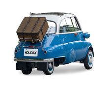 A Small Retro Car With A Suitcase Attached To The Back Is Ready For A Trip, Isolated On A White Background.