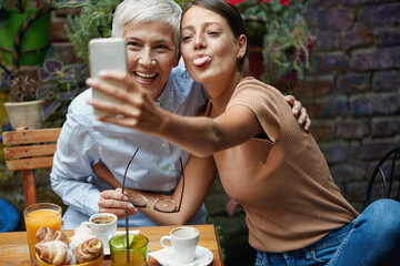 Wall Mural - A young girl is making funny faces while taking a selfie with her grandma at a bar. Leisure, bar, friendship, outdoor