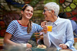 different age female friends concept. young woman laughing loud with elderly caucasian woman, sitting in outdoor cafe.
