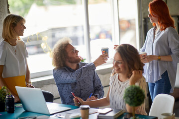 Group of young creative colleagues enjoying coffee while working in the office together