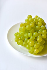 Green juicy delicious grapes on a white plate