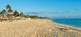 Fototapeta Tęcza - Cayo Coco, Cuba, 16 may 2021: Sandy beach of the hotel Tryp Cayo Coco with sun loungers and tall palm trees. People relax and sunbathe near the ocean on sun loungers.