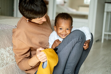 Caring caucasian woman hugging pretty African American baby boy, mother playing with her little son on the floor, family, adoption program