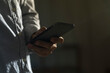© bennnn - Close-up of man using mobile phone for searching information in internet. Persons hand holding smartphone on dark background.