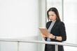 © EduLife Photos - Portrait of a cheerful confident Asian businesswoman in a business suit standing whie using a digital tablet in the business building. Business stock photo