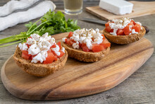 Burley Rusks With Chopped Tomatoes And Feta Cheese Served On Wooden Cutting Board. Greek “Dakos” Traditional Food Recipe.