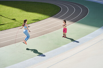 Wall Mural - Woman looking at her best friend skipping rope during sunny morning on stadium
