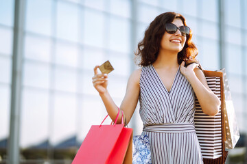 Cheerful woman enjoying shopping.  Fashion woman with shopping bags walking on street. Consumerism, sale, purchases, shopping, lifestyle concept.