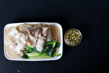 Top view of Fried noodle with pork in gravy sauce chinese style in white dish and glass bowl of slice green chilli in vinegar on black background in Thailand.