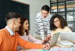 © insta_photos - Four diverse multiracial young happy cheerful coworkers business startup gen z creative team students brainstorming discussing online project with Asian mentor leader in classroom office using laptop.