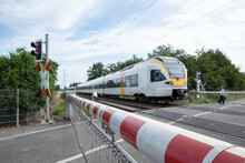 Selective Focus View At Red And White Level Crossing Railway Barrier Which Block The Road And Regional Train Move On The Rail On Countryside In Germany.	