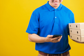 Wall Mural - Excited delivery service man smiling wearing blue uniform hold paper containers for takeaway pizza boxes packet and show smartphone blank screen, studio shot isolated on yellow background