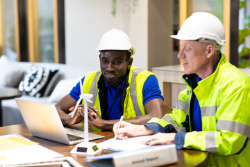 Wall Mural - Two engineers African american engineer and caucasian electrician wearing white hard hat working on laptop computer at workplace office. clean and green alternative energy concept.