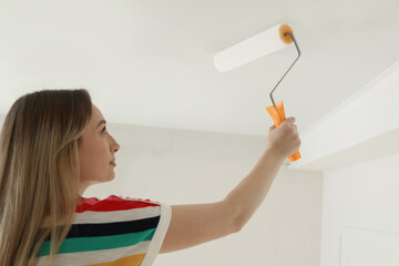 Wall Mural - Young woman painting ceiling with white dye indoors