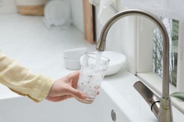 Poster - Woman filling glass with water from tap in kitchen, closeup