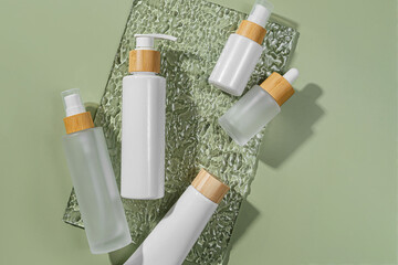 Pump bottle, cream tube, and dropper on green background. Cosmetic container mock-ups. Background for branding and packaging presentation. Natural skincare beauty product concept.