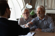 © fizkes - Happy grateful elderly couple of clients thanking real estate agent, lawyer, broker for help with house buying or selling, medical treatment contract, insurance agreement signing, giving handshake