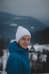 Candid portrait of a boy with a childish joyful smile in a winter white hat and blue jacket. Real portrait of a natural smiling teenager in winter months. No filter. Enjoy his life. Beskydy mountains