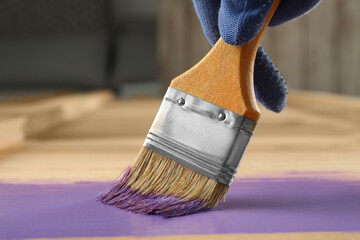 Worker applying violet paint onto wooden surface, closeup