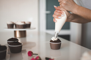 Woman decorate  homemade creamy chocolate cup cakes with cream stay on kitchen table close up. Preparation for birthday or wedding day