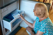 © ausra - Senior woman putting handkerchiefs in the fridge freezer. How to stay cool in hot weather.
