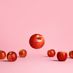 Wall Mural - Red and ripe apples placed in a row with one flying and levitating apple isolated on a bright pink background. Summer or fall fruit, delicious and healthy snack. Creative food concept.