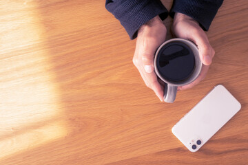 flat view, two hands holding a cup of coffee. beside smartphone. solo
